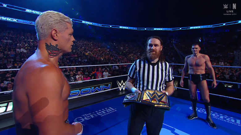 Rhodes and GUNTHER staring each other down in the ring as Zayn stands between them