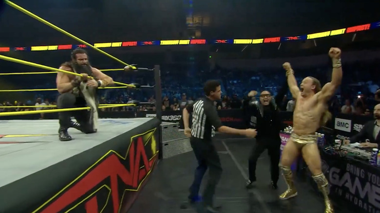 Mr. Elegance celebrating his win on the outside with The Personal Concierge as Elijah stands in the ring
