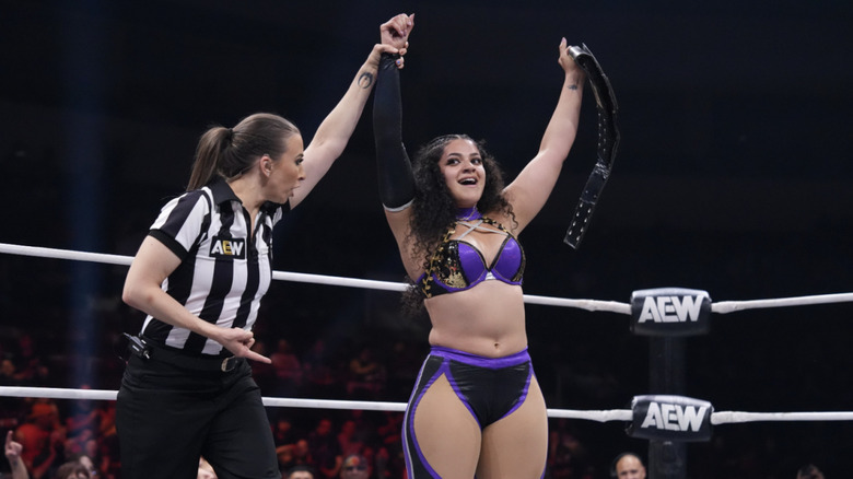 The referee raising Persephone's arm in the ring