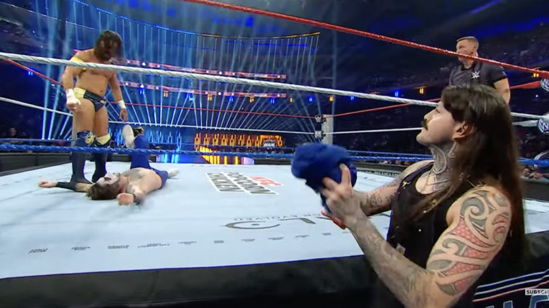 Dominik with Danhausen's custom jersey in hand as McDonagh stands over Danhausen in the ring