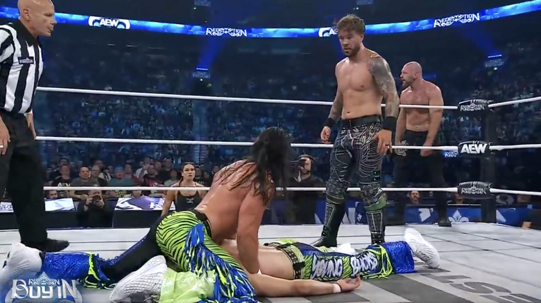 Matt shielding Nick in the ring as Ospreay stands over them and Moxley watches from the ring apron