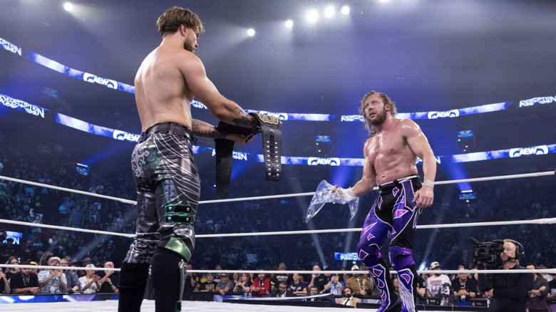 Ospreay with the AEW World Championship belt as Omega holds a ripped plastic bag